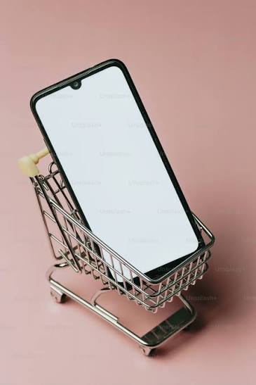 Phone with a white screen inside a miniature shopping cart on a pink background